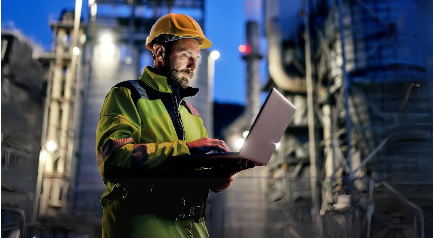 Photo of an engineer on his laptop in front of a chemical plant