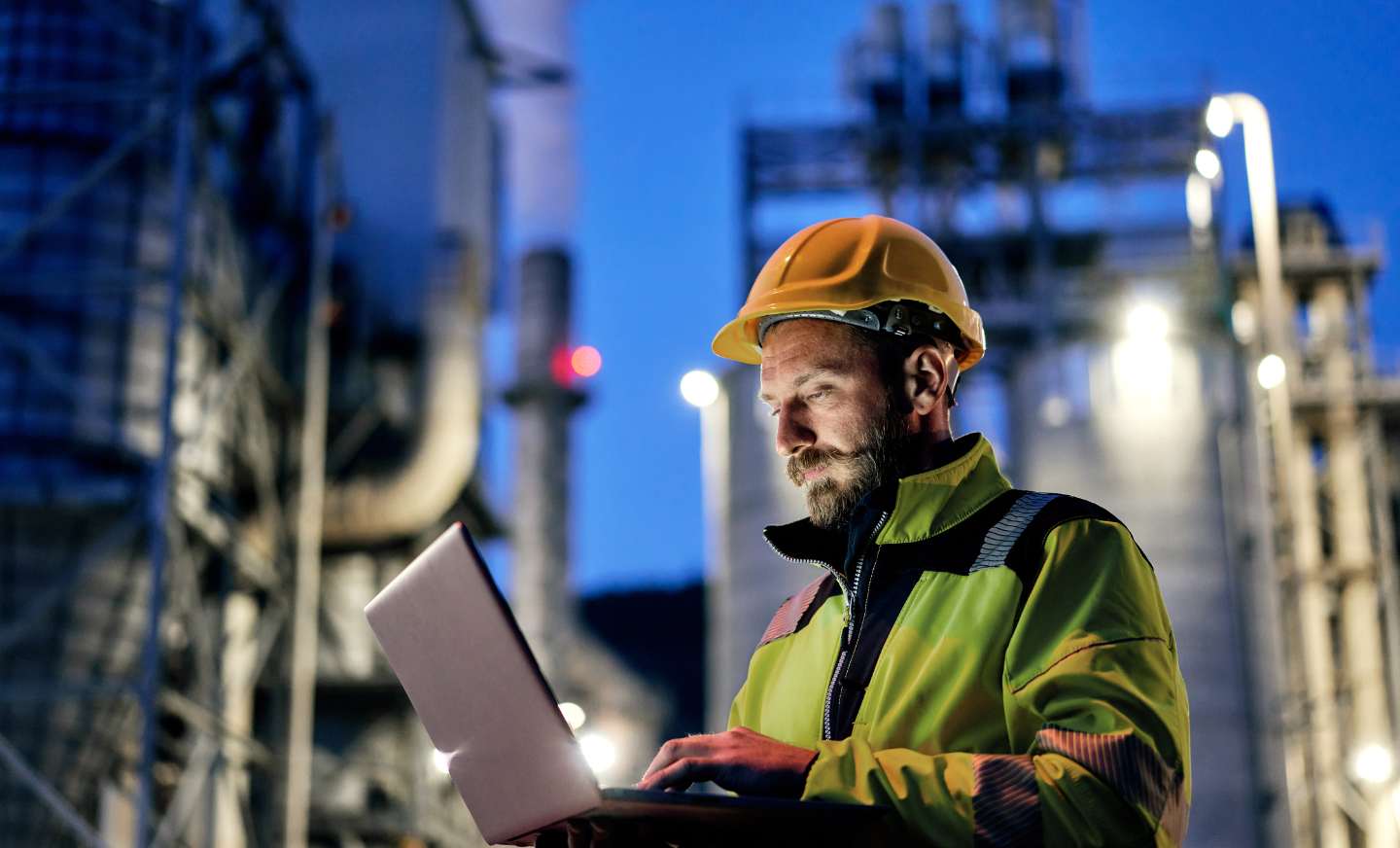 an engineer working on his laptop in front of a oil plant